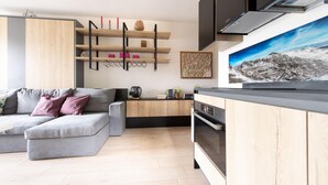 A modern living room with a grey sofa, wooden cabinets, and a kitchen area with a stove and oven. - Italianway - Bagni Nuovi 12 (Valdidentro)