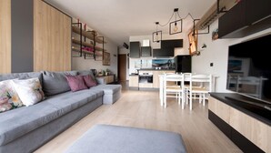 A modern living room with a grey sofa, white dining table, and chairs. There is a kitchen area with a stove and cabinets. - Italianway - Bagni Nuovi 12 (Valdidentro)