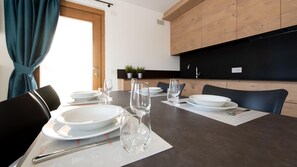 A dining table set with plates, glasses, and cutlery in a modern kitchen with wooden cabinets and a black countertop.