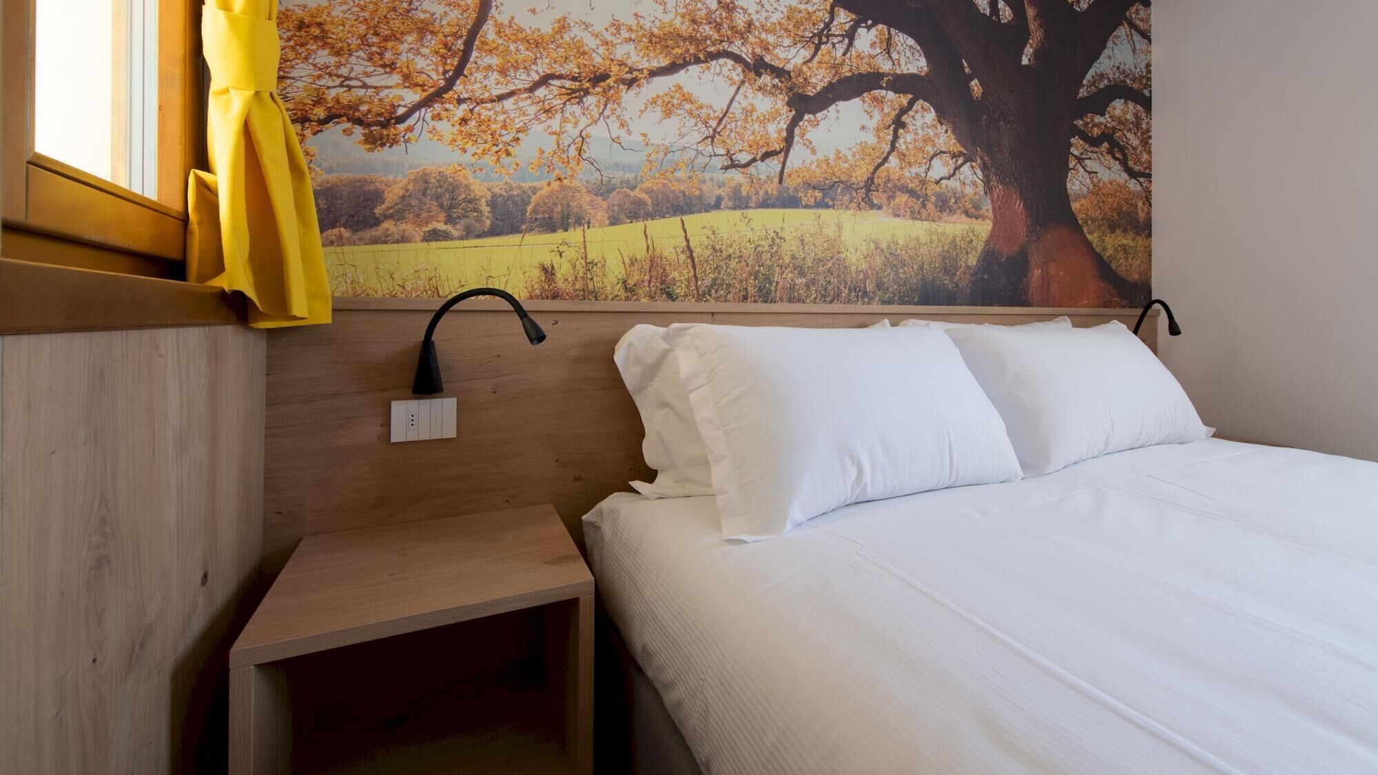 A bedroom with a wooden headboard, a bedside table, a lamp, and a bed with white bedding.