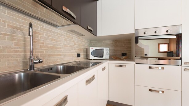 A modern kitchen with stainless steel appliances, a brick backsplash, and white cabinetry. - Italianway - Funivie 6A (Bormio)