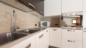 A modern kitchen with stainless steel appliances, a brick backsplash, and white cabinetry. - Italianway - Funivie 6A (Bormio)