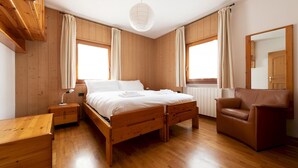 A wooden-paneled bedroom with a bed, bedside tables, a chair, and a mirror. - Italianway - Funivie 6A (Bormio)