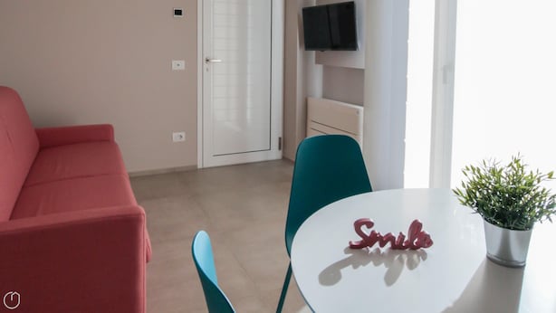 A modern living room with a red sofa, teal chairs, a white table with a potted plant, and a flat-screen TV mounted on the wall. - Villa Paloma - Levante Bs-e967-prov4at (Marone)