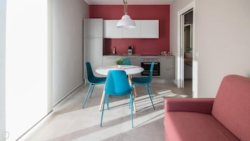 Una cocina moderna con armarios blancos, una pared de acento roja y un comedor con sillas azules y una mesa blanca.