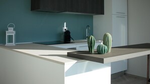 A modern kitchen with a minimalist design, featuring a dark backsplash, a coffee machine, and decorative cacti. - Villa Paloma - Scirocco Bs-e967-prov4c1 (Marone)