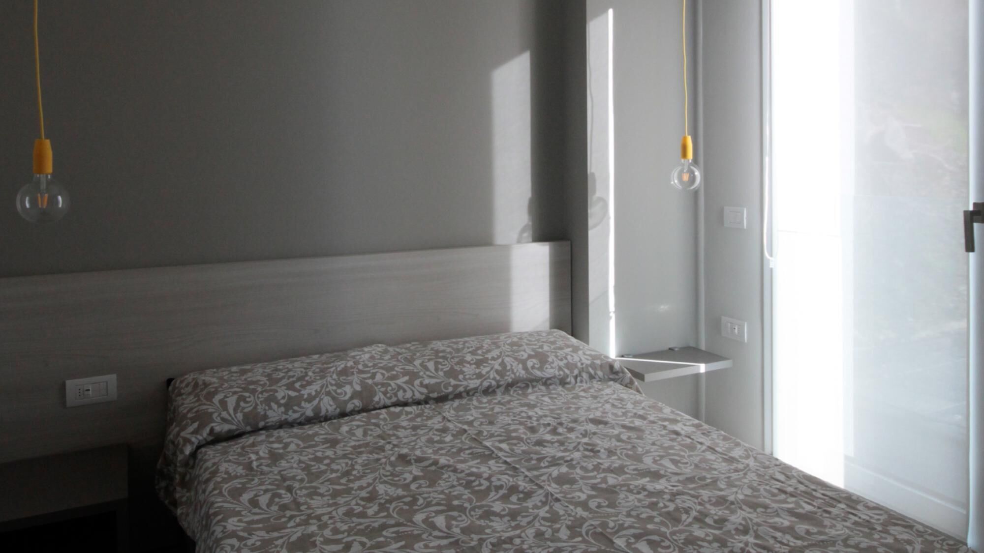 A bedroom with a bed, a bedside table, a window, and two hanging light fixtures.
