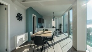 A modern kitchen with a large island, a dining area with a wooden table and black chairs, and a large sliding glass door leading to a balcony with a view. - Villa Paloma - Scirocco Bs-e967-prov4c1 (Marone)