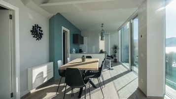Una cocina moderna con una isla grande, un comedor con mesa de madera y sillas negras, y un amplio ventanal corredero que da a un balcón con vistas.