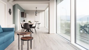 A modern living room with a sofa, a small table, and a dining area with chairs and a table. - Villa Paloma - Scirocco Bs-e967-prov4c1 (Marone)