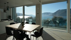 A modern dining area with a large table and chairs, large windows offering a view of a lake and mountains. - Villa Paloma - Scirocco Bs-e967-prov4c1 (Marone)
