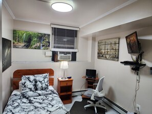 A bedroom with a bed, desk, chair, and a wall-mounted TV.