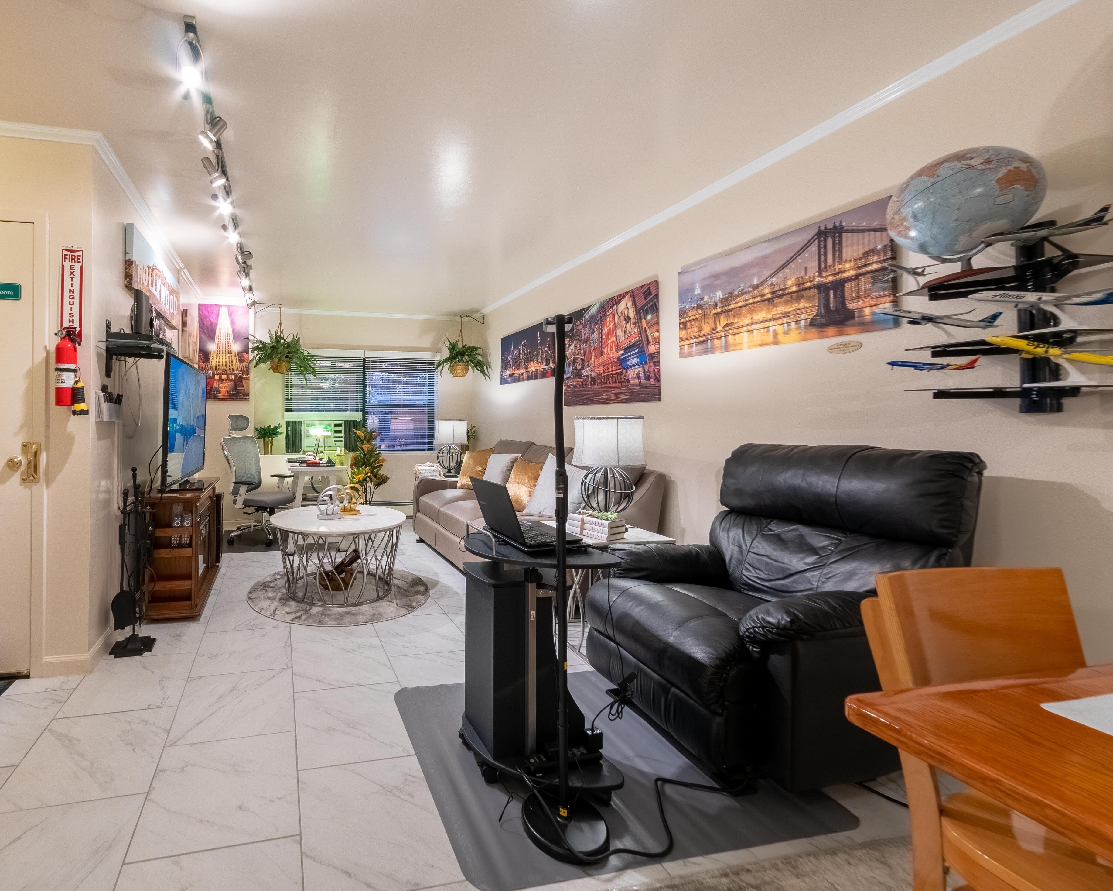 Un salon moderne avec un canapé en cuir noir, une table à manger et un téléviseur. On y trouve également des objets décoratifs et un globe terrestre accroché au mur.