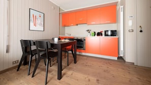 A compact kitchen with orange cabinets, a microwave, a kettle, and a toaster. There is a dining table with chairs and a framed picture on the wall. - Italianway - Cacciatori Delle Alpi 7 (Bormio)