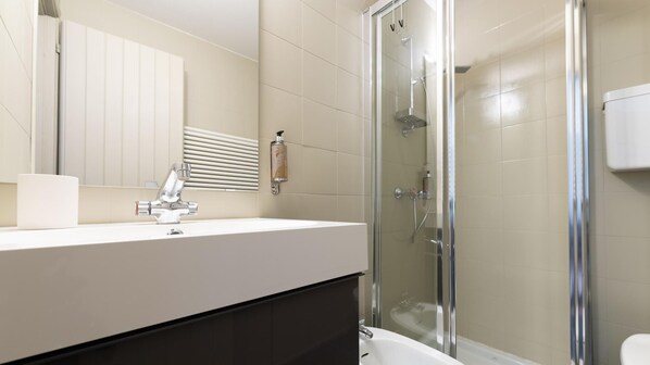 A modern bathroom with a glass-enclosed shower, a white sink with a chrome faucet, and a large mirror above the vanity. - Italianway - Cacciatori Delle Alpi 7 (Bormio)