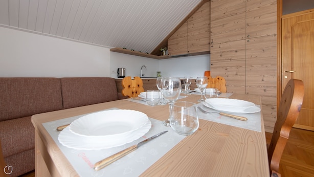 A dining area with a wooden table set for four, a brown sofa, and a kitchen in the background. - Italianway - Besta 2 (Bormio)