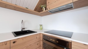 A modern kitchen with a black sink, stainless steel faucet, wooden cabinets, a built-in oven, and a black countertop. - Italianway - Besta 2 (Bormio)