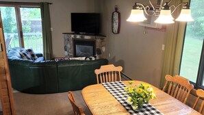 A dining area with a wooden table, checkered table runner, and chairs. A television is mounted above a stone fireplace, and a clock is on the wall. - Lakes-area vacation - walk to Pelican Lake, golfing, bars, restaurants and more! (Pequot Lakes)