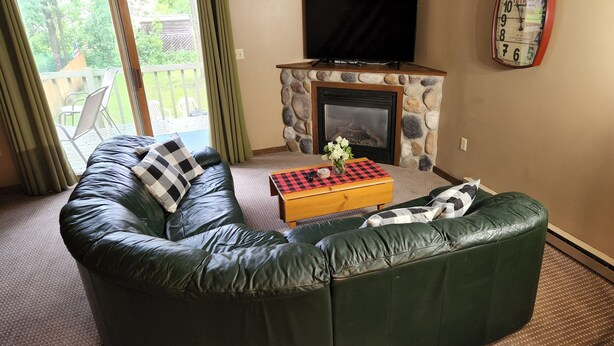 A living room with a green leather sofa, a checkered ottoman, a flat-screen TV, and a stone fireplace. - Lakes-area vacation - walk to Pelican Lake, golfing, bars, restaurants and more! (Pequot Lakes)