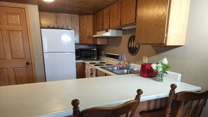 A kitchen with wooden cabinets, a white refrigerator, a microwave, a toaster, and a sink. There are two wooden chairs at the kitchen island. - Lakes-area vacation - walk to Pelican Lake, golfing, bars, restaurants and more! (Pequot Lakes)