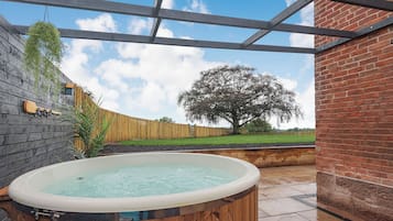Un bain à remous situé dans un espace extérieur abrité, agrémenté d’une clôture en bois, d’un arbre et d’un mur en briques.