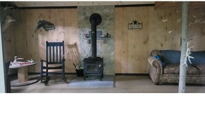 Een gezellige kamer met een houten wand, een stenen openhaard, een houten stoel, een bank en een welkomstbord.