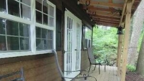 Een houten veranda met twee metalen stoelen en een tafel, een houten hek en een metalen dakconstructie.