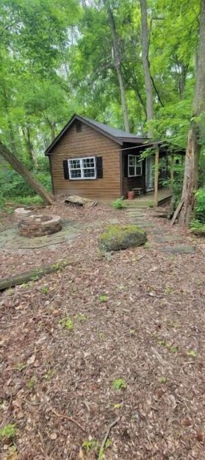 A wooden cabin with a porch, surrounded by dense forest.