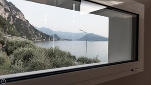 A view through a window of a lake with mountains in the background and a bridge on the left. - Villa Paloma - Maestrale Bs-e967-prov4d2 (Marone)