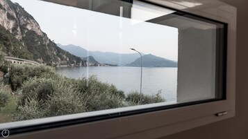Vista a través de una ventana que muestra un lago con montañas al fondo y un puente a la izquierda.