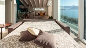 A bedroom with a large bed, two pillows, a view of a dining area, and a balcony overlooking a body of water. - Villa Paloma - Maestrale Bs-e967-prov4d2 (Marone)