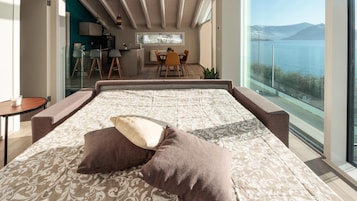 Un dormitorio con una cama grande, dos almohadas, vista a un comedor y un balcón con vistas al agua.