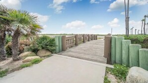 Een houten pad dat leidt naar een omheind gebied met palmbomen en groen.