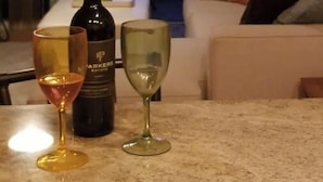 Een woonkamer met uitzicht op een zonsondergang, een fles wijn en twee glazen op een tafel.