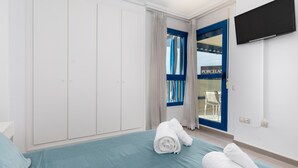 Habitación de hotel con una cama, un televisor montado en la pared y vista al exterior a través de una puerta con cortinas.