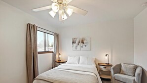 Une chambre d’hôtel comprenant un lit, une chaise, un bureau, un ventilateur de plafond et deux lampes fixées au mur.