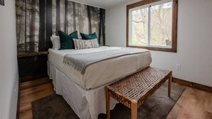 Een slaapkamer met een bed, kussens, een bankje, een raam en een muur met een bosdecoratie.