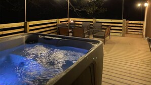 Een hottub op een houten terras met sfeerverlichting erboven.