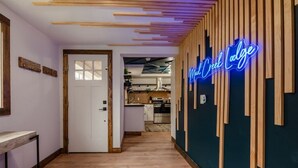 Een gang met houten vloer, een neonbord waarop 'Mud Creek Lodge' staat en een deur naar een keuken.