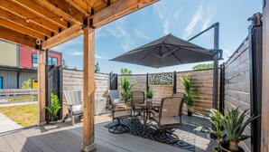 Eine überdachte Terrasse mit Tisch, Stühlen, einem Sonnenschirm und Blumentöpfen.