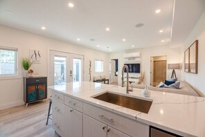 A modern kitchen with a large island, a built-in sink, and a dining area with a sofa. - FLX Solar Powered Village/Tunnel to Seneca Lake! (Geneva)