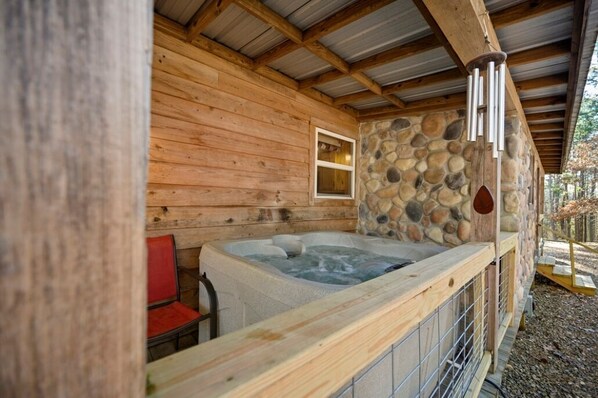 A wooden cabin with a stone wall, a hot tub, and a red chair.