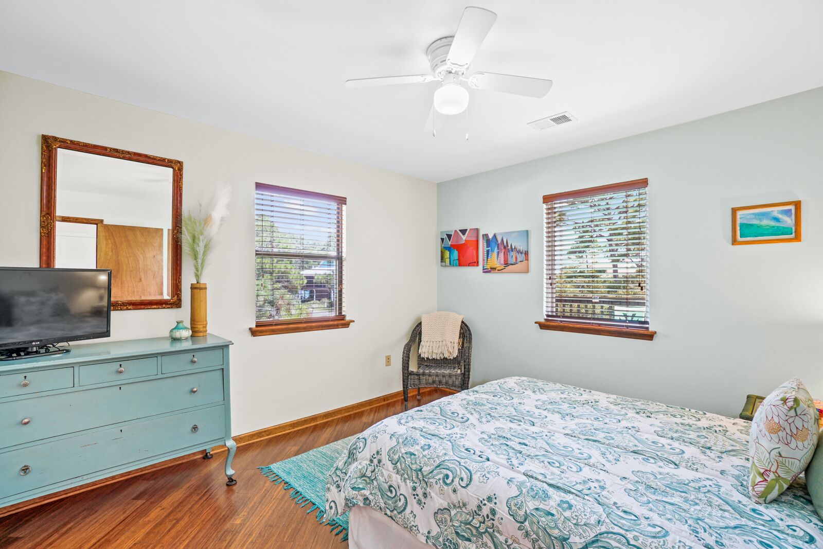 Une chambre à coucher comprenant un lit, une commode, un téléviseur et un ventilateur de plafond.
