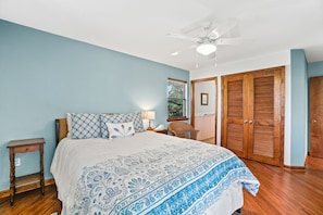 A bedroom with a bed, a nightstand, a chair, a window with blinds, and a ceiling fan.