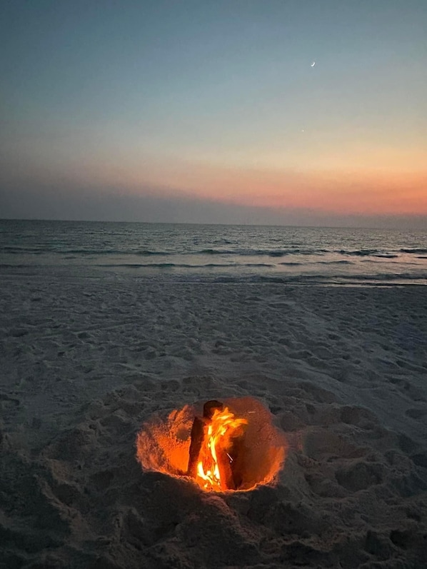A beach scene with a fire pit in the sand.