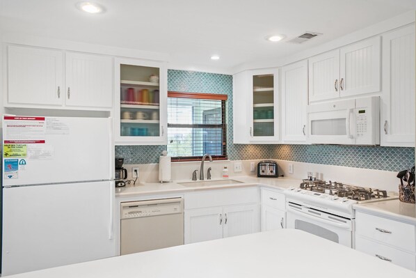 A modern kitchen with white cabinetry, a built-in dishwasher, a stove, and a microwave. - Vacation Rental in Beach-Front Neighborhood with Pool Access (Port St. Joe)
