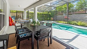 Eine überdachte Terrasse mit Pool, Esstisch, Stühlen und Liegestühlen.