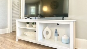 Un mueble blanco de entretenimiento con un televisor de pantalla plana, estantes con objetos decorativos y una puerta con diseño de ladrillo blanco.