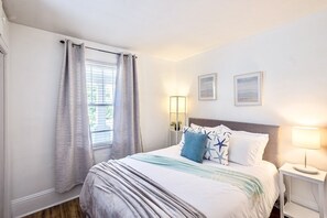 Ein Schlafzimmer mit Bett, Vorhängen, einer Nachttischlampe und zwei an der Wand befestigten Bilderrahmen.
