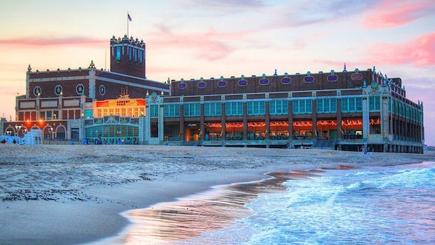 Un hotel frente a la playa con una imponente torre de reloj, un edificio grande con múltiples ventanas, y una playa en primer plano.